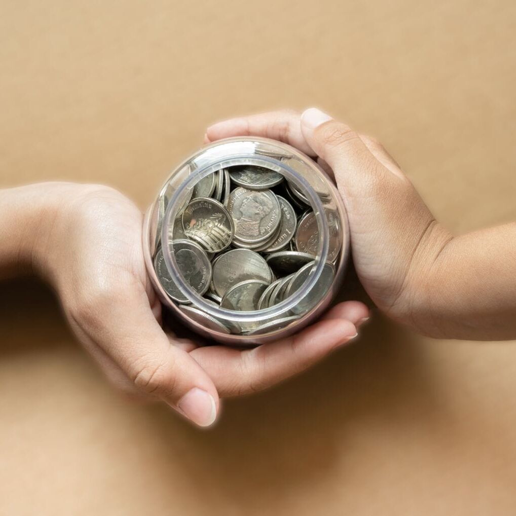 Kid hands holding coins in a jar together as saving concept for family or education. Saving concept using kid hands holding coins.
